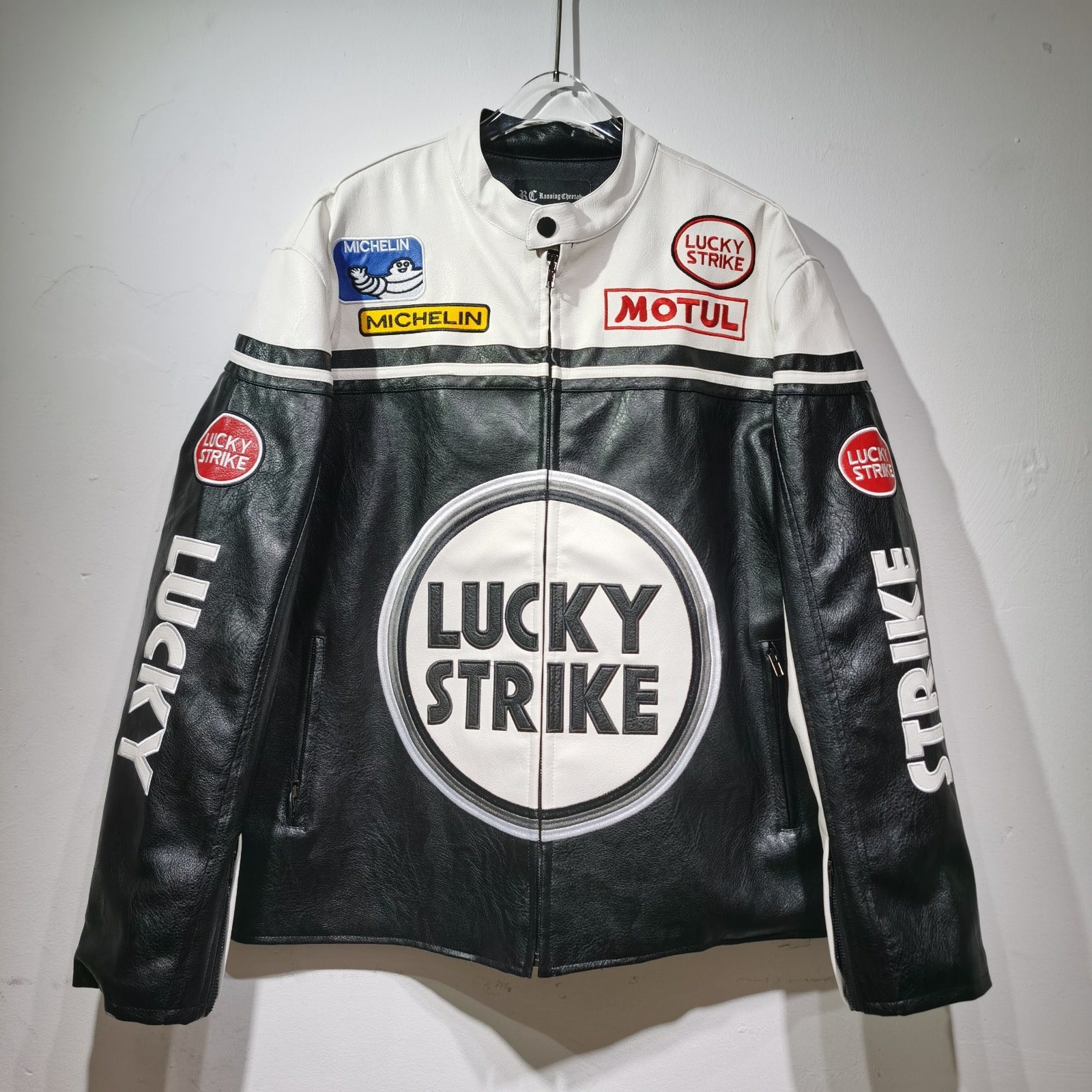 Black and white leather jacket with Lucky Strike branding on a hanger against a gray background