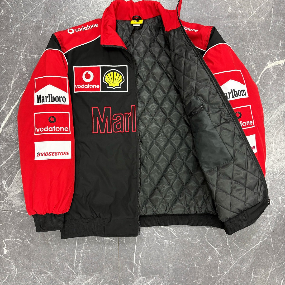 Red and black quilted jacket with various logos on a gray marble surface