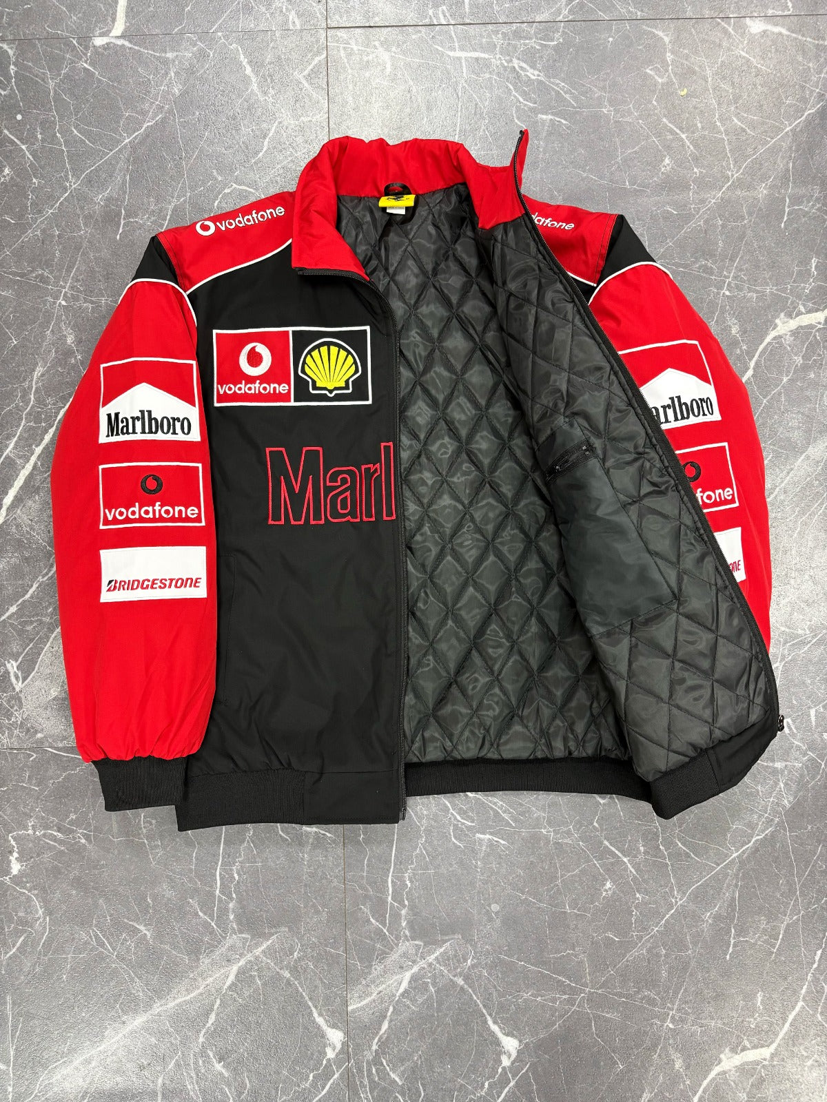 Red and black quilted jacket with various logos on a gray marble surface