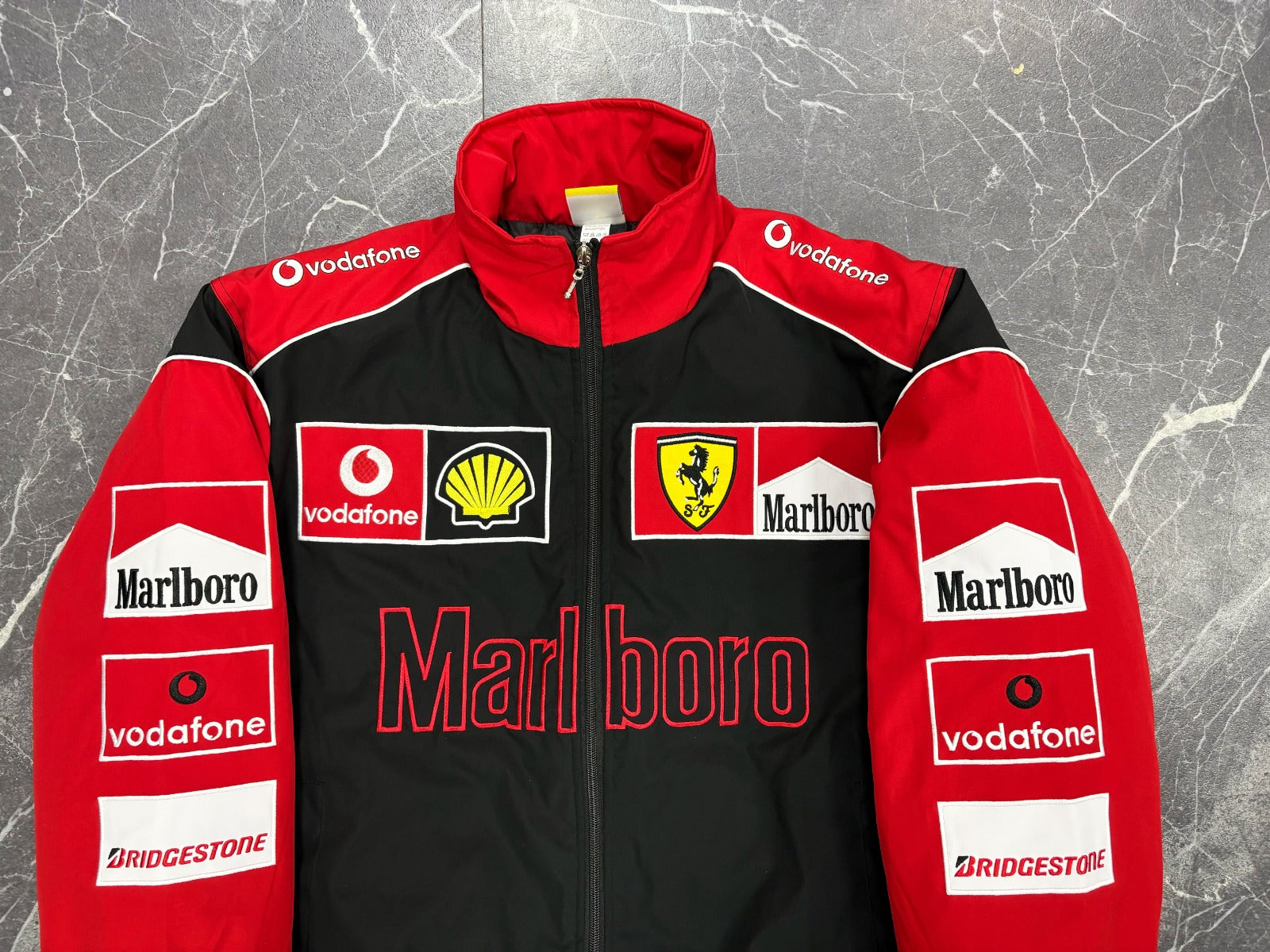Red and black jacket with various sponsor logos on a textured gray background