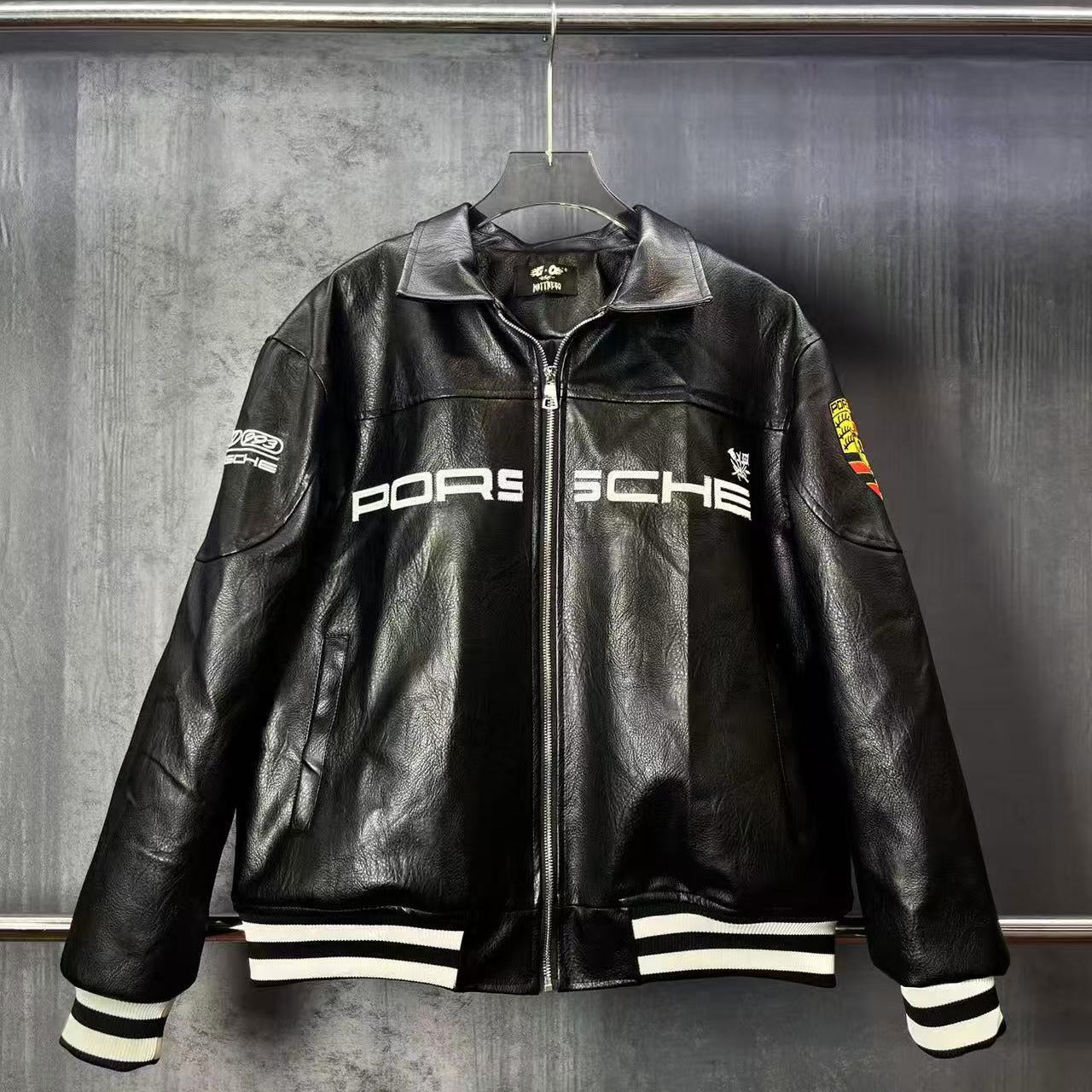 Black leather Porsche jacket on a hanger against a dark background