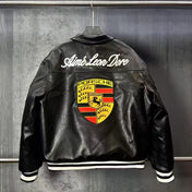 Black leather jacket with Porsche logo and 'Aime Leon Dore' text on a metallic surface.