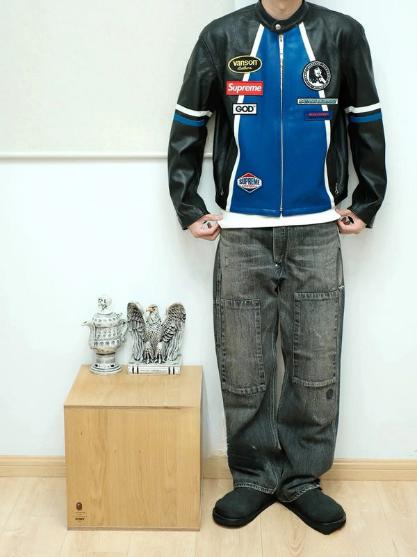 Person wearing a black and blue leather jacket with various logos, standing next to a wooden box with decorative items.