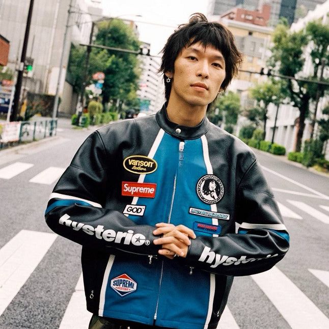 Person wearing a jacket with various brand logos on a city street