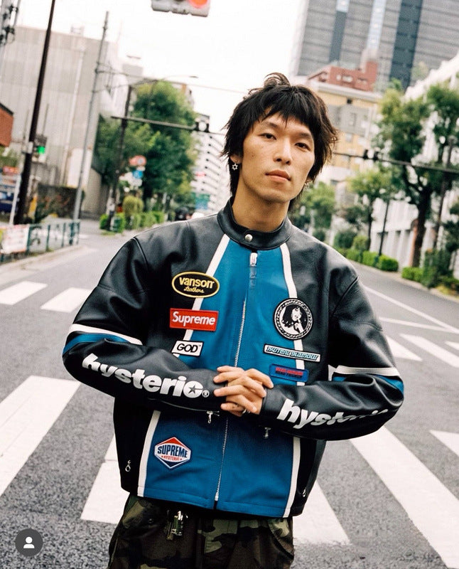 Person wearing a jacket with various brand logos on a city street