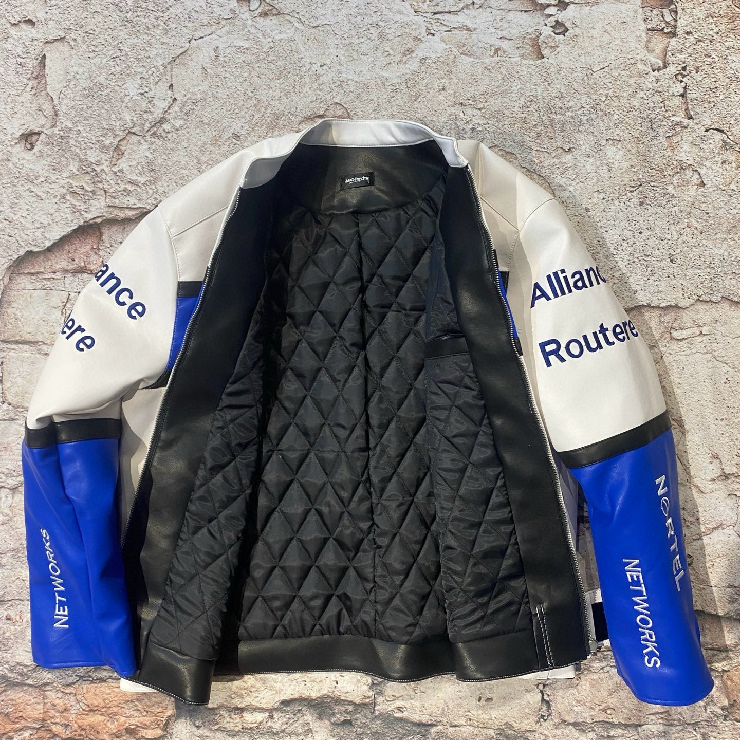 Black quilted jacket with blue and white sleeves against a textured stone wall.