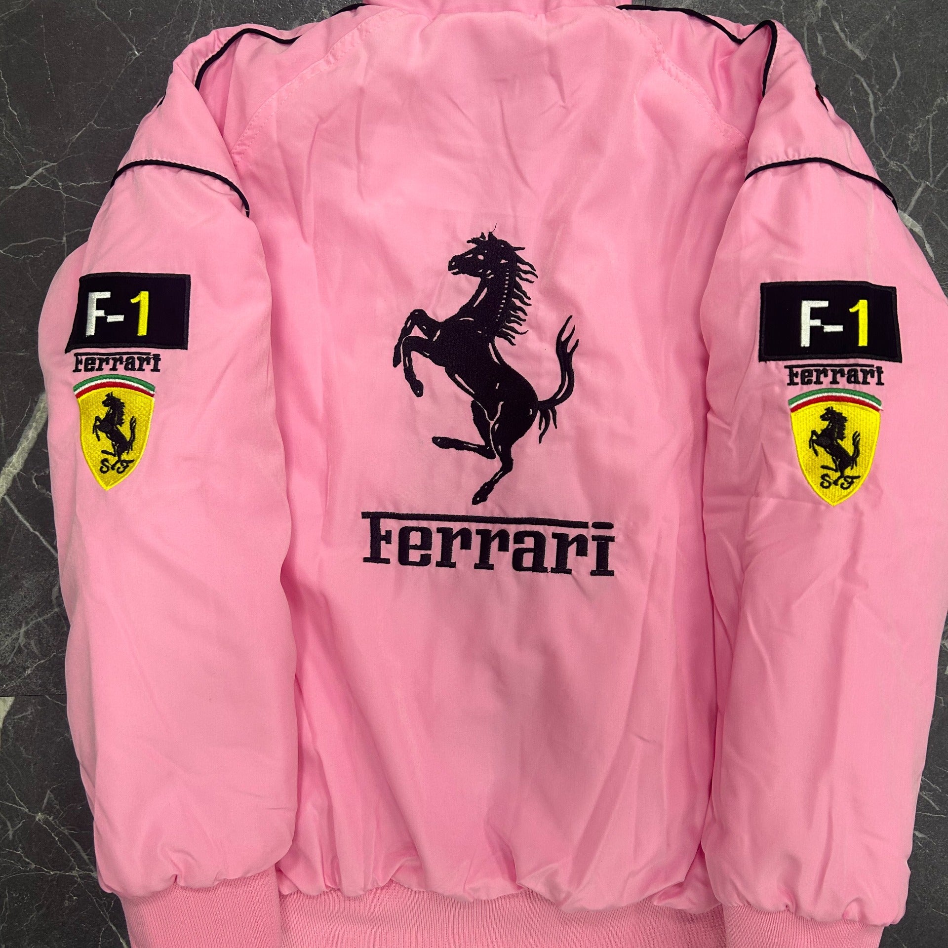 Pink Ferrari jacket with logo and branding on a dark textured background