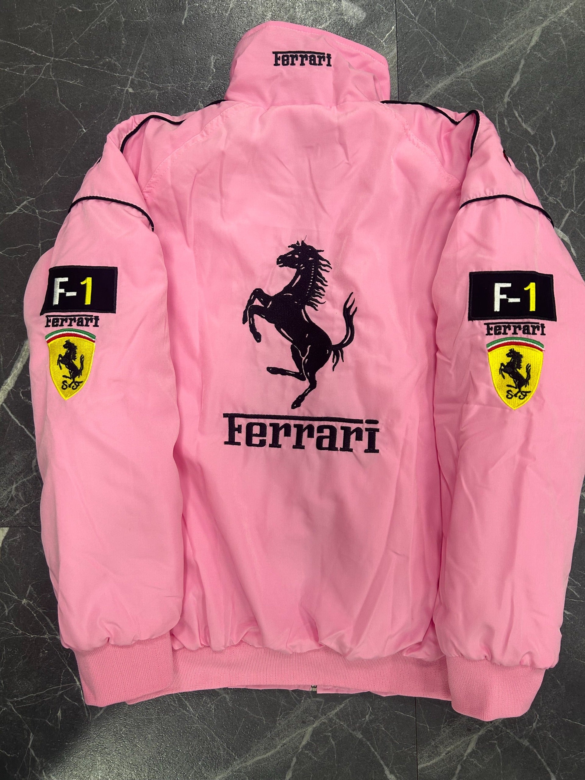 Pink Ferrari jacket with logo and branding on a dark textured background