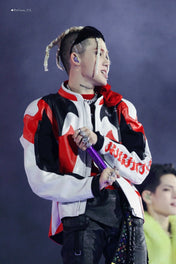 Person wearing a red, black, and white jacket with a purple object in hand against a dark background