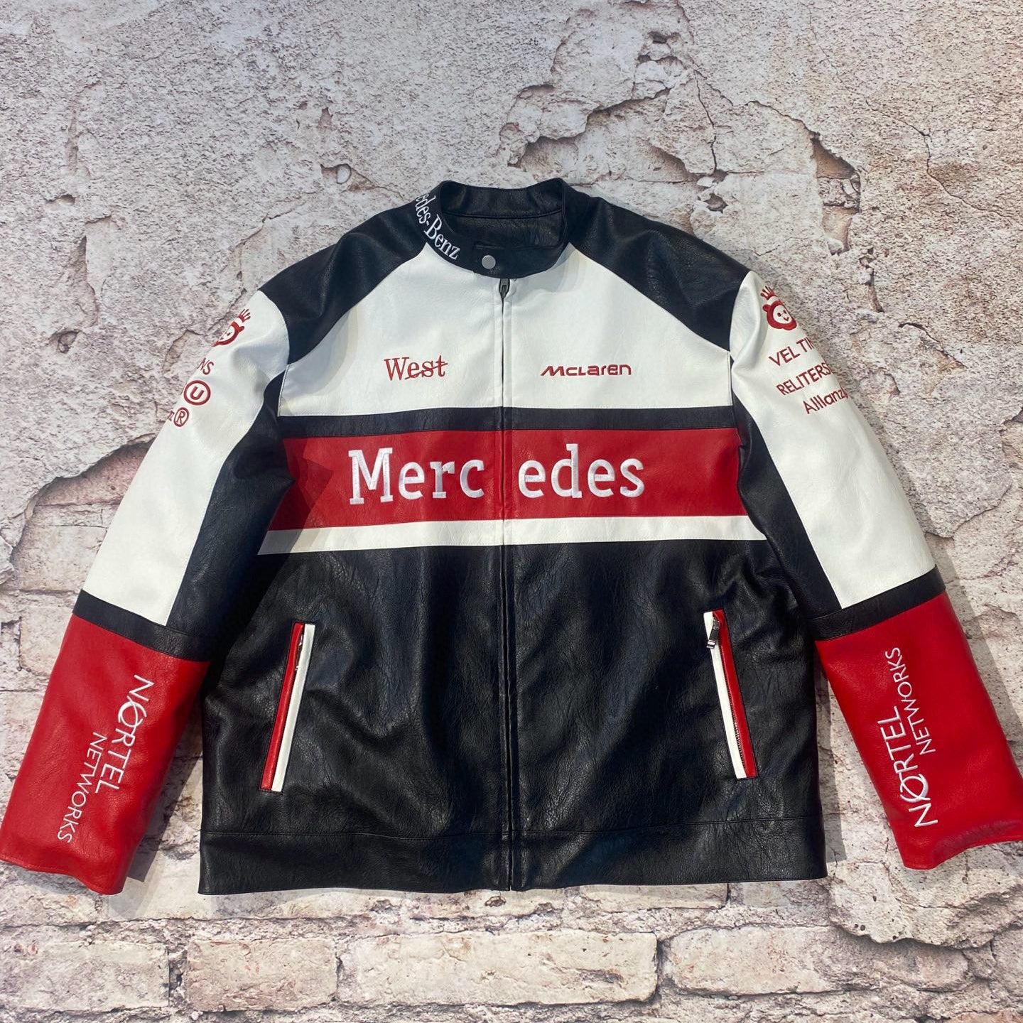 Black, white, and red racing jacket with Mercedes branding on a textured stone background