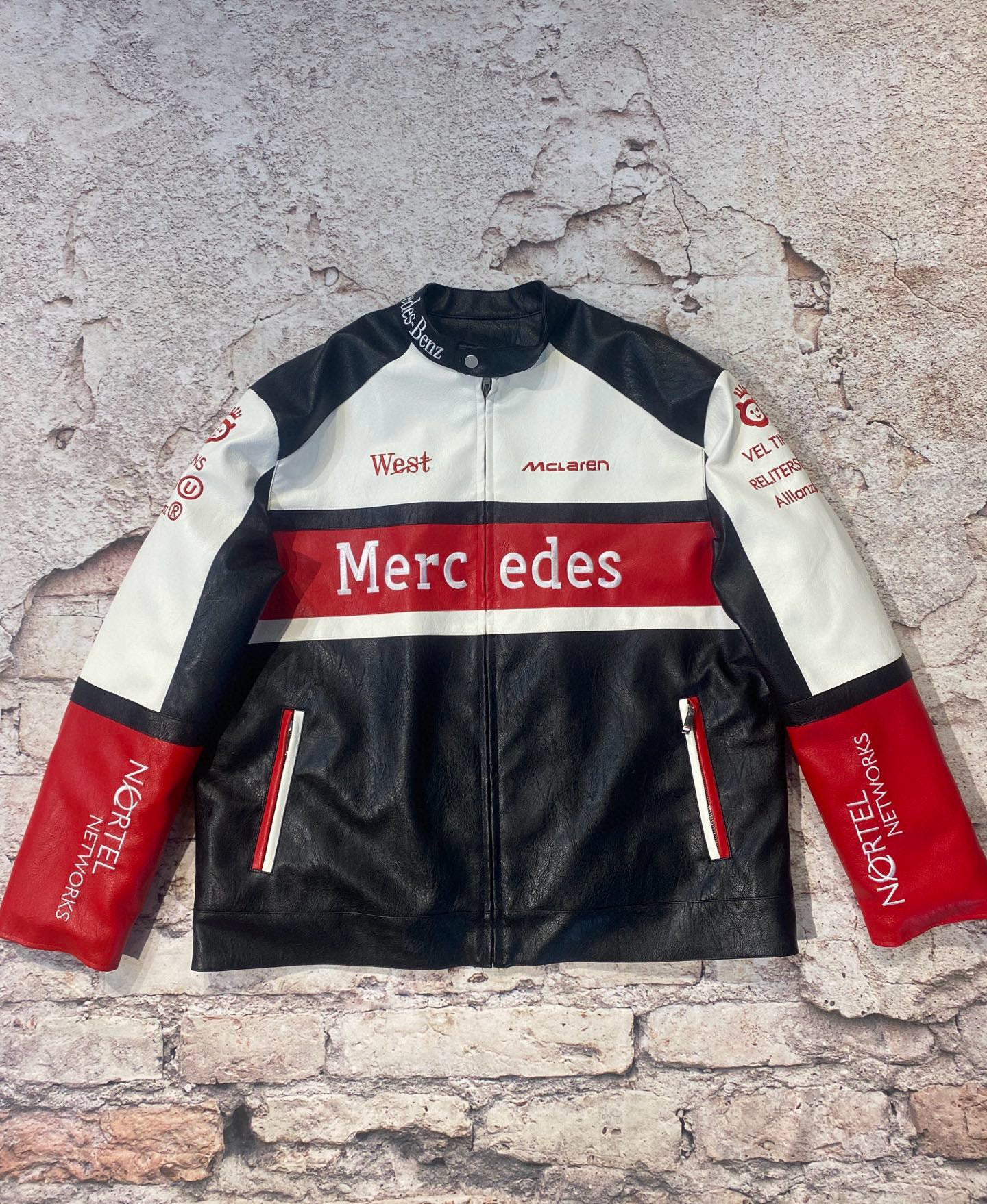 Black, white, and red racing jacket with Mercedes branding on a textured stone background