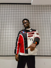 Person wearing a colorful jacket with brand logos against a grid-patterned wall.