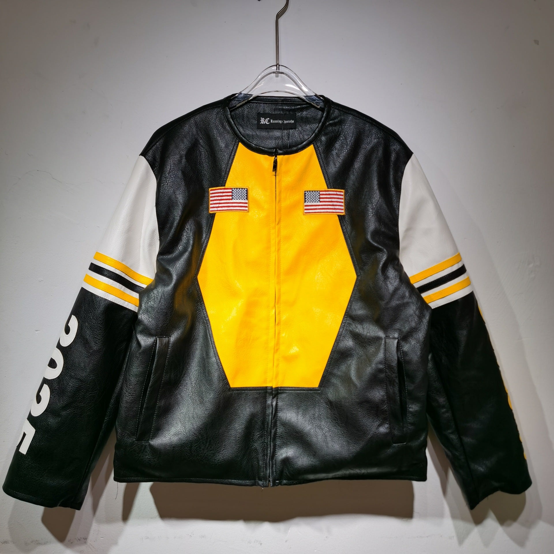 Black leather jacket with yellow center and white sleeves on a hanger against a gray background