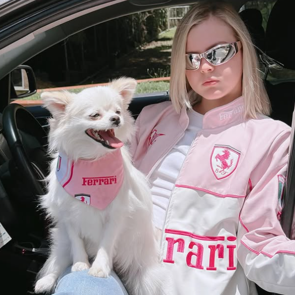 Person and dog in a car wearing matching Ferrari-themed outfits