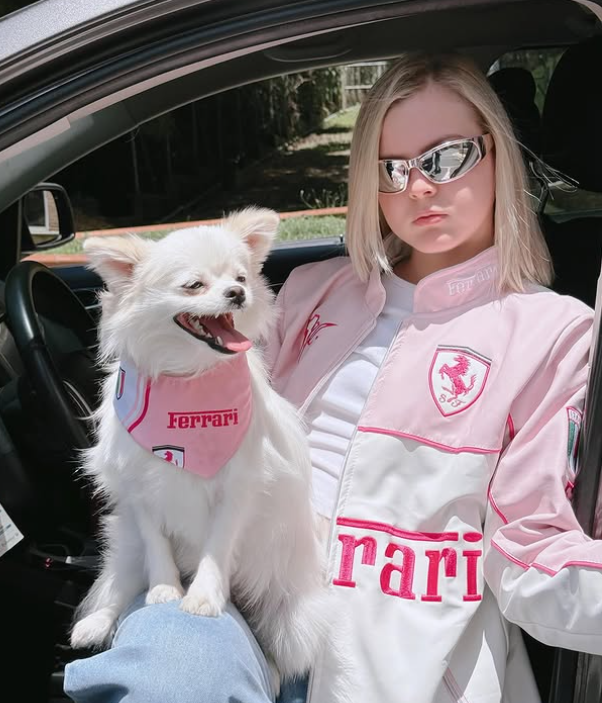 Person and dog in a car wearing matching Ferrari-themed outfits