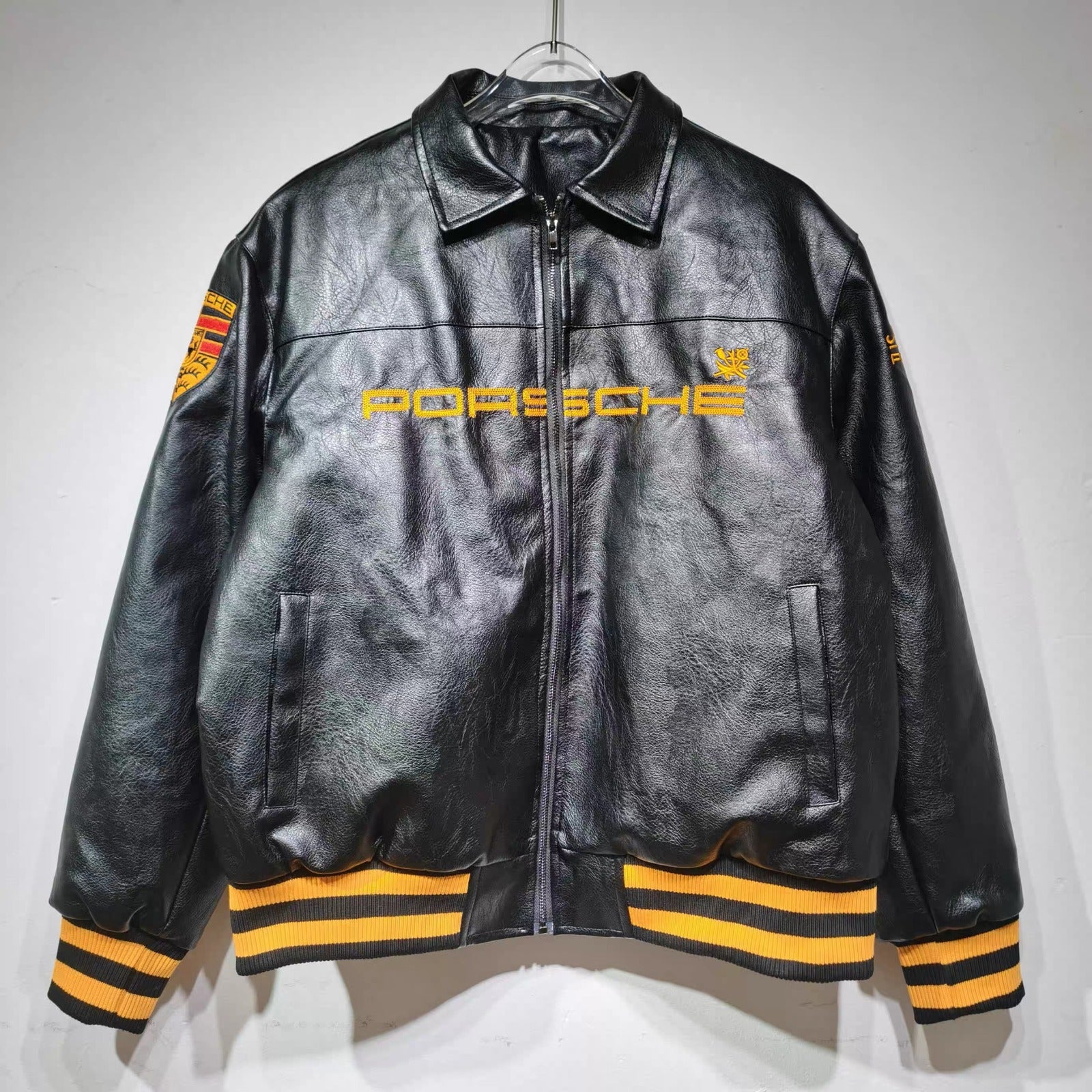 Black leather jacket with yellow accents and Porsche logo on a white background