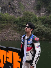 Person wearing a colorful jacket with sponsor logos near a body of water and rocky cliff.