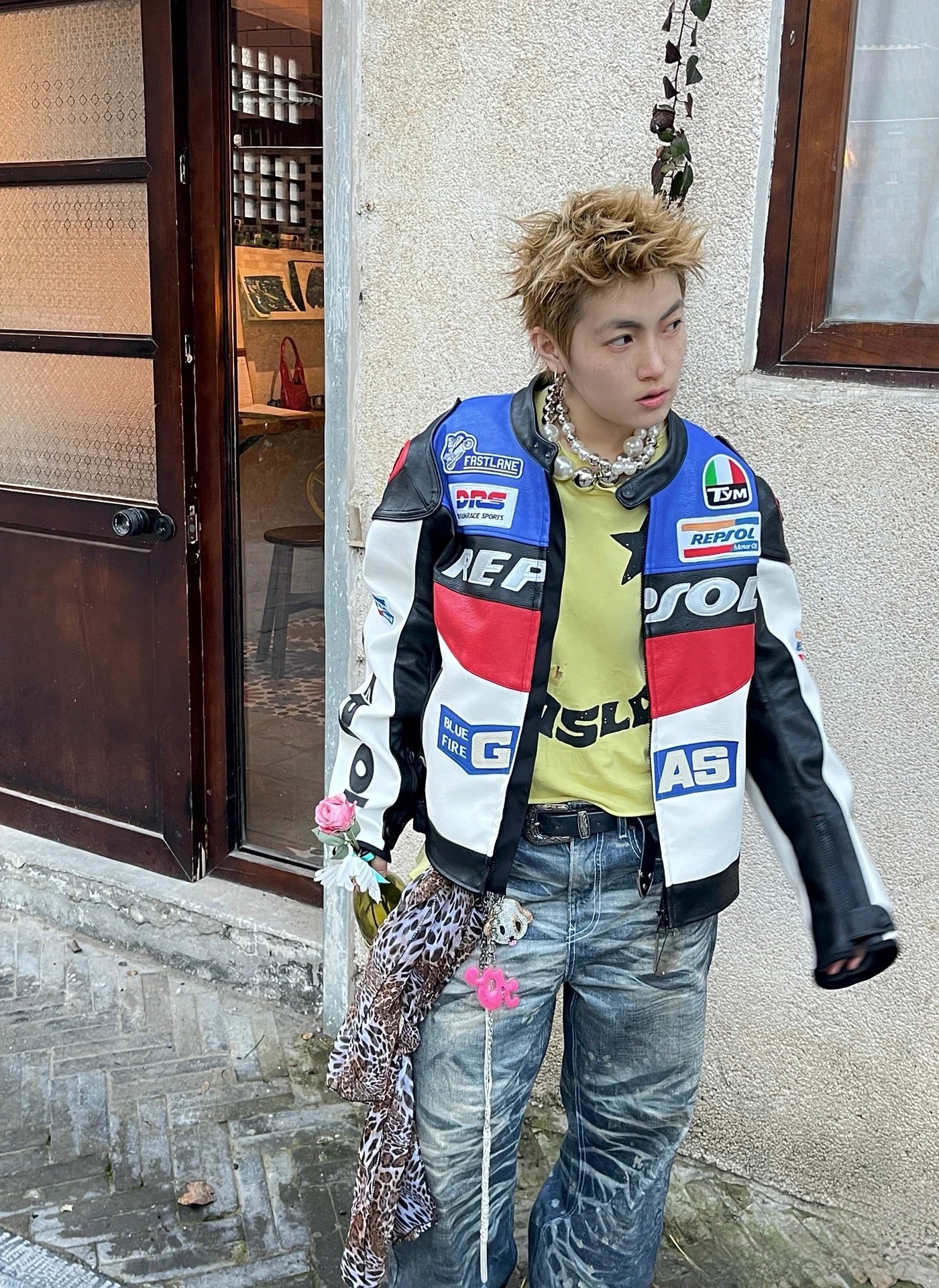 Person wearing a colorful jacket with various logos, standing against a building exterior.